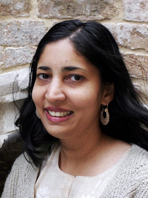Die Schriftstellerin Kiran Desai steht lächelnd vor einem mittelalterlichen Mauerwerk. Die Schriftstellerin Kiran Desai steht lächelnd vor einem mittelalterlichen Mauerwerk.