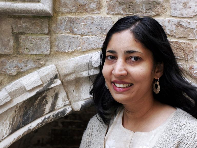Die Schriftstellerin Kiran Desai steht lächelnd vor einem mittelalterlichen Mauerwerk. Die Schriftstellerin Kiran Desai steht lächelnd vor einem mittelalterlichen Mauerwerk.
