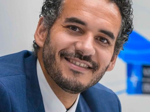 Dominik Wullers trägt einen blauen Anzug, eine altrosa Krawatte und schaut freundlich in die Kamera.