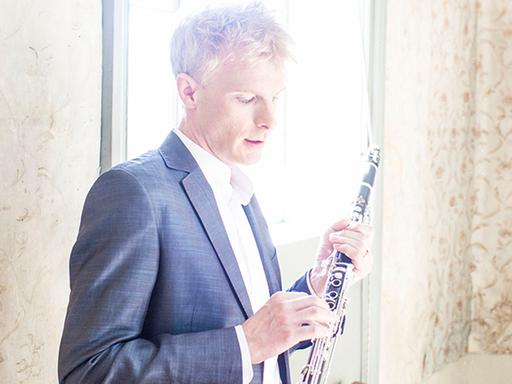 Martin Fröst steht vor einem viel Licht gebenden Fenster mit seinem Instrument, das er liebevoll in den Händen hält.