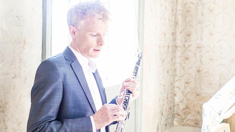 Martin Fröst steht vor einem viel Licht gebenden Fenster mit seinem Instrument, das er liebevoll in den Händen hält.