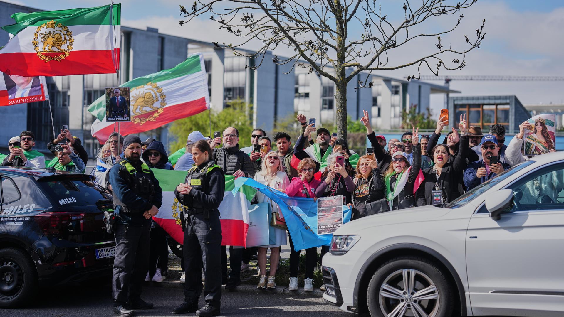 Polizisten stehen vor einer Gruppe, in der Fahnen der iranischen Monarchie geschwenkt werden.