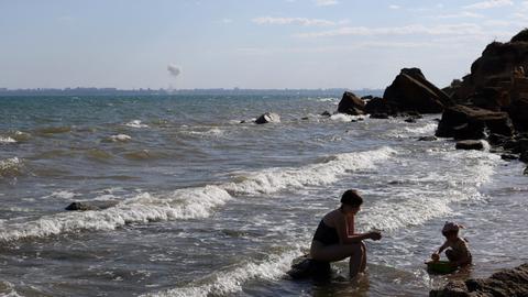Eine Mutter spielt mit ihrem Kind am Strand von Odessa, während am Horizont eine Bombe im Meer detoniert. Eine Mutter spielt mit ihrem Kind am Strand von Odessa, während am Horizont eine Bombe im Meer detoniert.