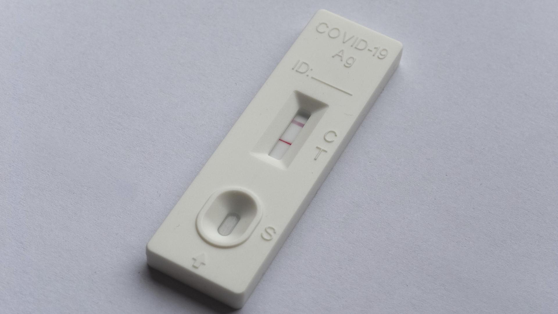 Ein positiver Covid 19 Antigen-Schnelltest liegt auf grauem Untergrund