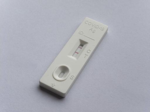Ein positiver Covid 19 Antigen-Schnelltest liegt auf grauem Untergrund