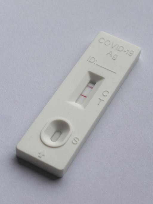 Ein positiver Covid 19 Antigen-Schnelltest liegt auf grauem Untergrund