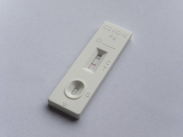 Ein positiver Covid 19 Antigen-Schnelltest liegt auf grauem Untergrund