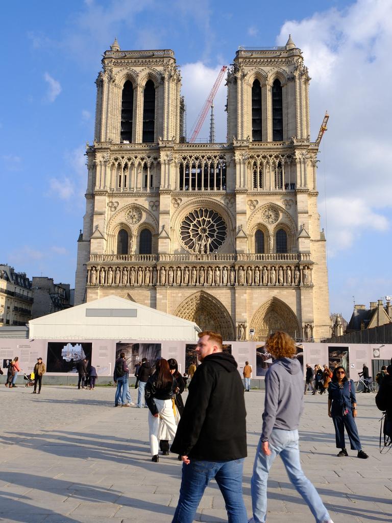Blick auf die Pariser Kirche Notre Dame: Auf dem Platz im Vordergrund sind herumlaufende Menschen zu sehen, hinter der Kirche ragen zwei Baukräne hervor.
