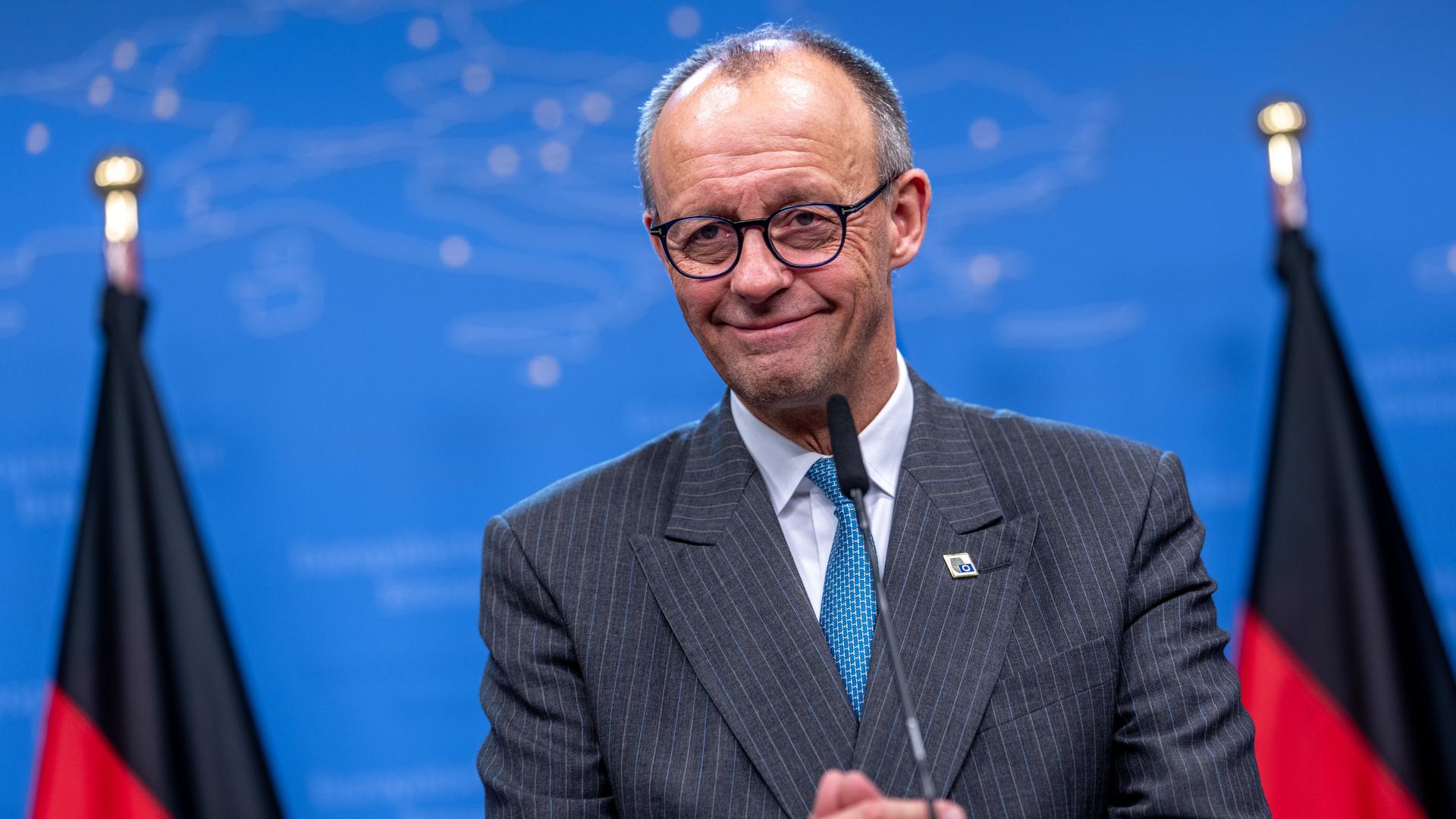Kanzler Merz steht bei einer Pressekonferenz vor einer blauen Wand. Er wird von Deutschlandfahnen eingerahmt. Kanzler Merz steht bei einer Pressekonferenz vor einer blauen Wand. Er wird von Deutschlandfahnen eingerahmt.