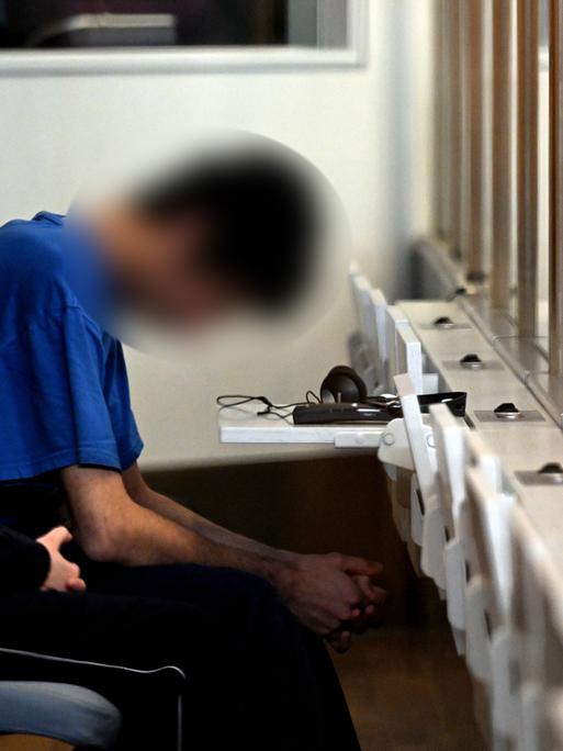 Der wegen Mordes in Solingen Angeklagte sitzt im Oberlandesgericht Düsseldorf mit tief gesenktem Kopf hinter einer Glasscheibe.