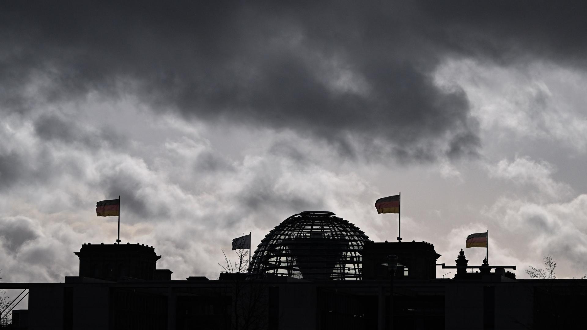 Wolken sind über der Kuppel vom Reichstag zu sehen, auf dem Deutschlandfahnen wehen.