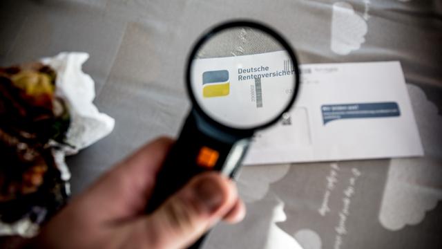 Eine Hand hält eine Lupe und vergrößert den Schriftzug "Deutsche Rentenversicherung", der auf einem Briefumschlag gedruckt ist.