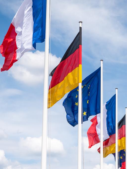 Mehrere Flaggen Frankreichs, Deutschlands und der EU wehen unter leicht bewölktem Himmel