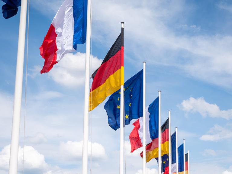 Mehrere Flaggen Frankreichs, Deutschlands und der EU wehen unter leicht bewölktem Himmel