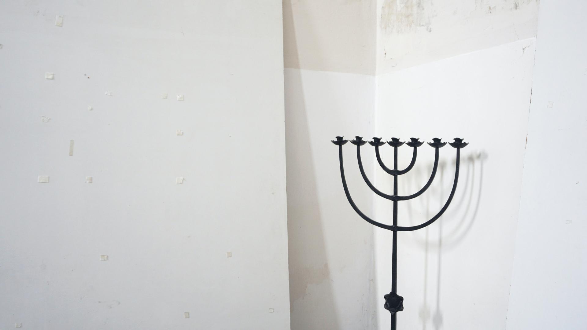 Ein siebenarmiger Leuchter, eine sogenannte Menorah, steht vor einer weißen Wand.