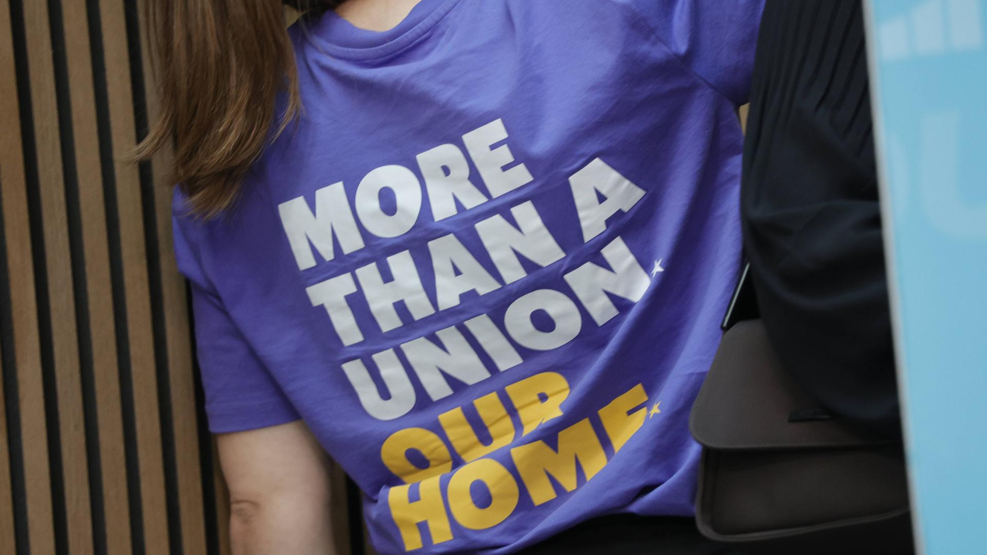 Eine Frau trägt ein lila T-Shirt mit der Aufschrift: "More than a Union - Our Home"