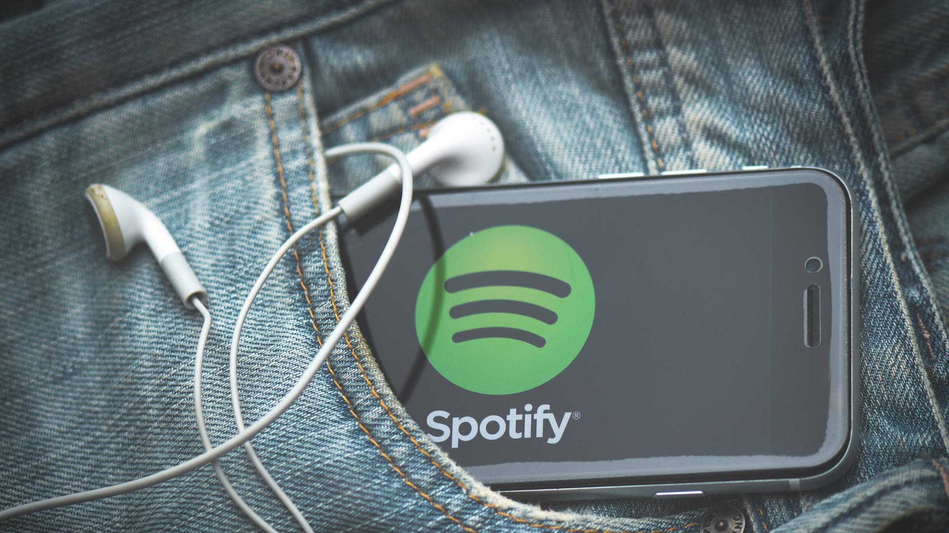 Ein Smartphone mit Spotify-App und Kabelkopfhörern schaut aus einer Jeans-Tasche heraus