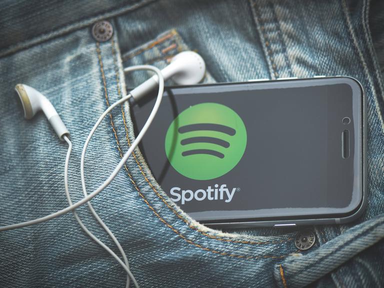 Ein Smartphone mit Spotify-App und Kabelkopfhörern schaut aus einer Jeans-Tasche heraus