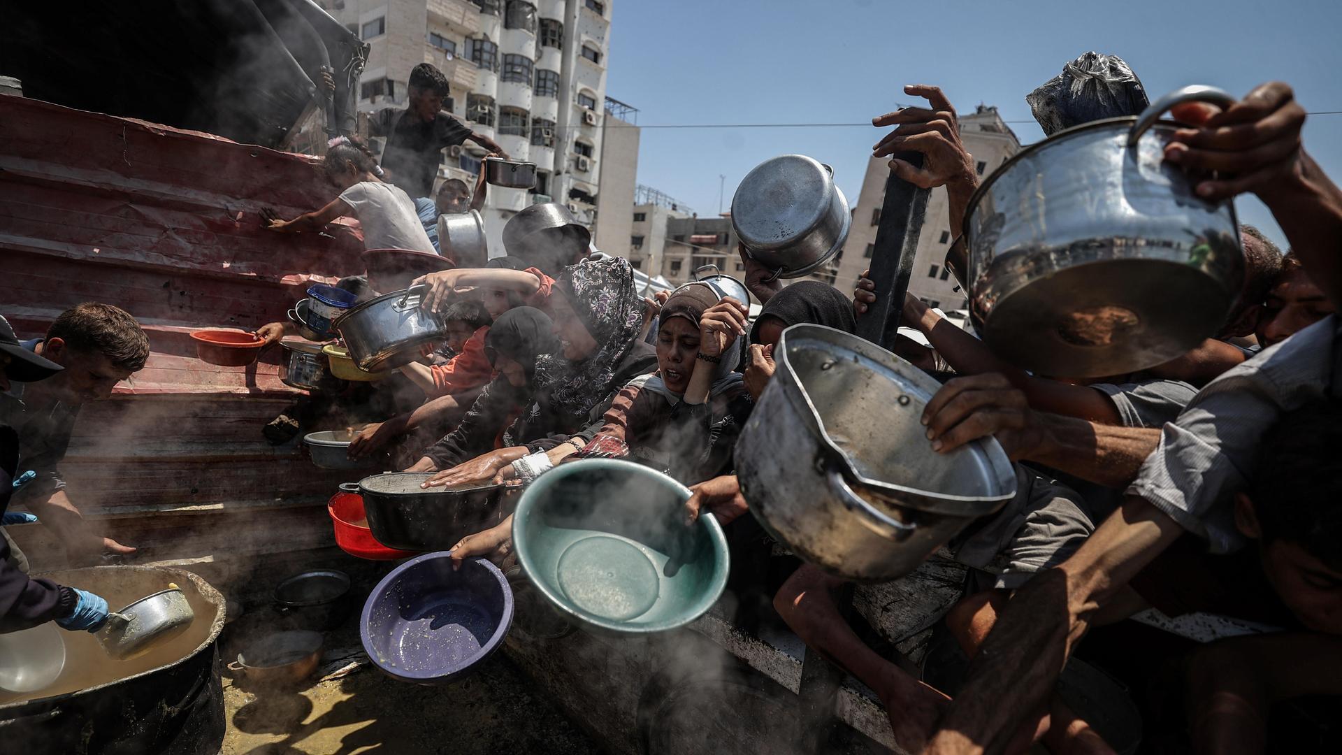Menschen im Gazastreifen halten an einer Essensausgabe Schüsseln und Töpfe in die Luft. Menschen im Gazastreifen halten an einer Essensausgabe Schüsseln und Töpfe in die Luft.