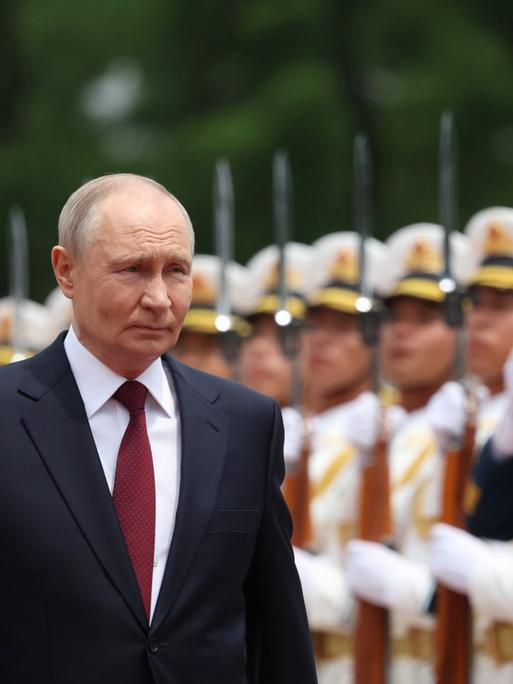 Wladimir Putin bei seinem jüngsten China-Besuch im Mai 2026. Er lächelt, im Hintergrund sind aufgereiht chinesische Soldaten zu sehen. 