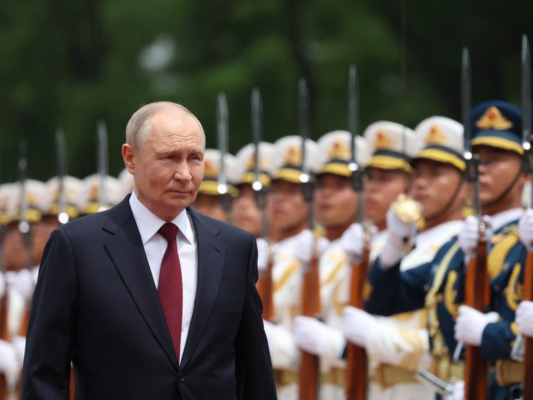 Wladimir Putin bei seinem jüngsten China-Besuch im Mai 2026. Er lächelt, im Hintergrund sind aufgereiht chinesische Soldaten zu sehen. 