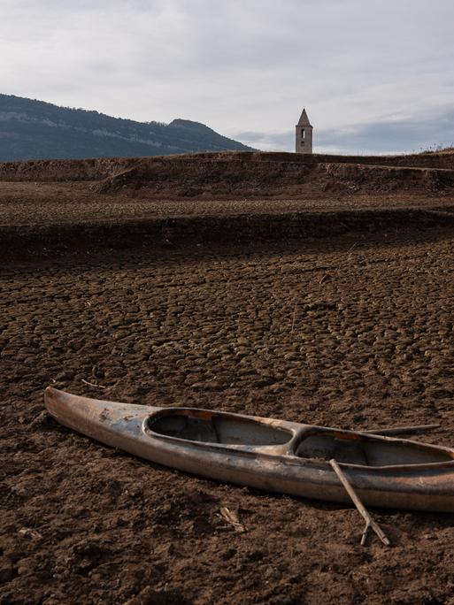 Ein ausgetrockneter Stausee in Katalonien: Im Vordergrund liegt ein Boot auf ausgetrockneter Erde, im Hintergrund sieht man einen Kirchturm