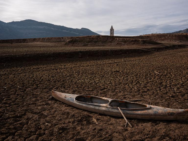 Ein ausgetrockneter Stausee in Katalonien: Im Vordergrund liegt ein Boot auf ausgetrockneter Erde, im Hintergrund sieht man einen Kirchturm