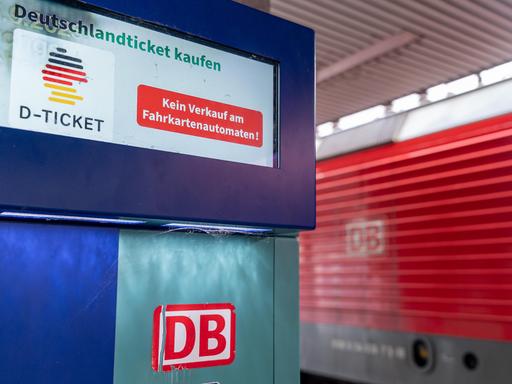 Ein Fahrkartenautomat der Deutschen Bahn mit Hinweis, dass das Deutschlandticket (D-Ticket) nicht am Automaten erhältlich ist. Im Hintergrund ist eine rote Lokomotive mit DB-Logo zu sehen.