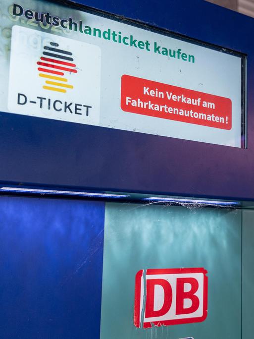 Ein Fahrkartenautomat der Deutschen Bahn mit Hinweis, dass das Deutschlandticket (D-Ticket) nicht am Automaten erhältlich ist. Im Hintergrund ist eine rote Lokomotive mit DB-Logo zu sehen.