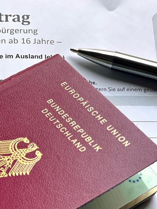 Ein Antrag auf Einbürgerung und ein deutscher Pass liegen auf einem Tisch.