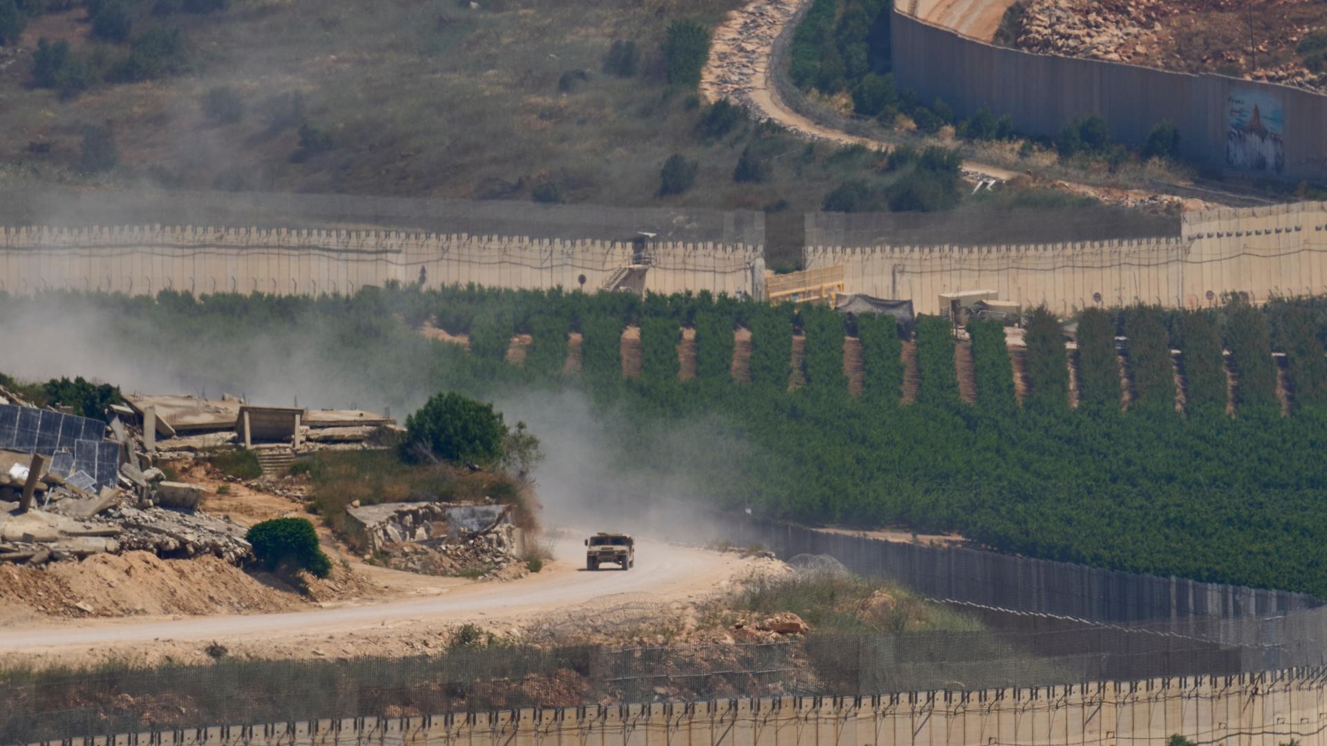Israel, Grenze von Israel zum Libanon: Ein israelisches Militärfahrzeug fährt an zerstörten Gebäuden im Südlibanon vorbei, aufgenommen aus Nordisrael. 