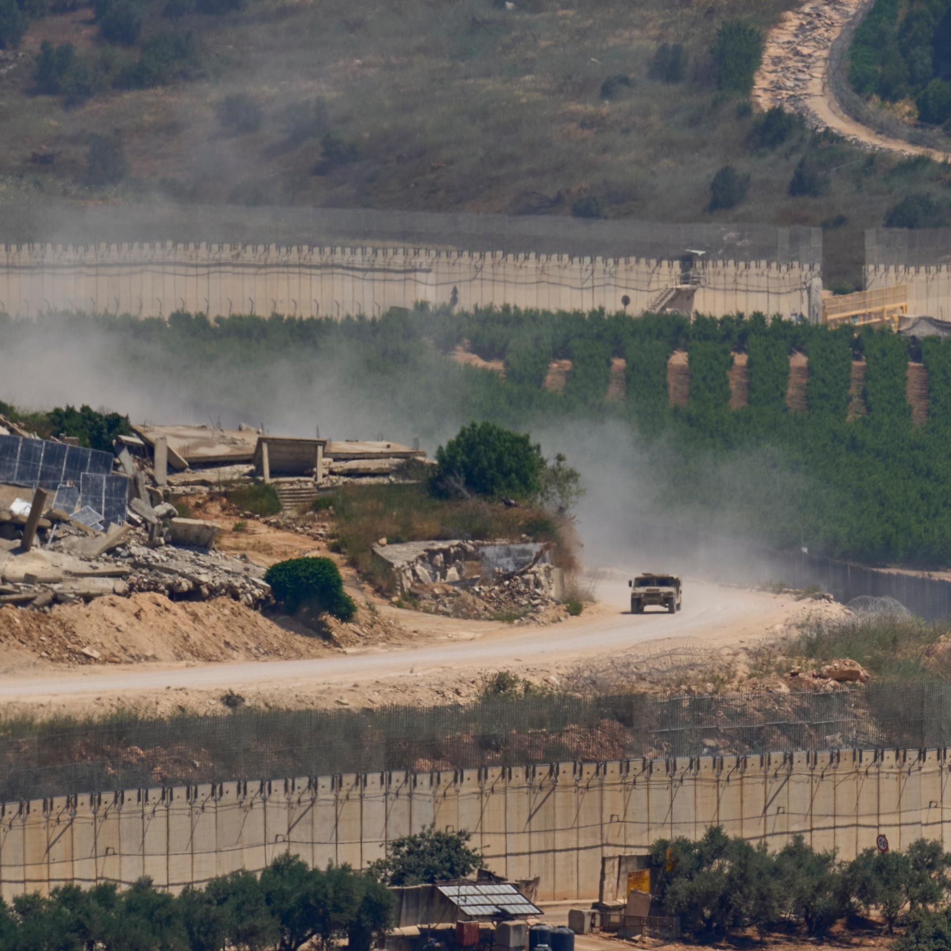 Israel, Grenze von Israel zum Libanon: Ein israelisches Militärfahrzeug fährt an zerstörten Gebäuden im Südlibanon vorbei, aufgenommen aus Nordisrael. 