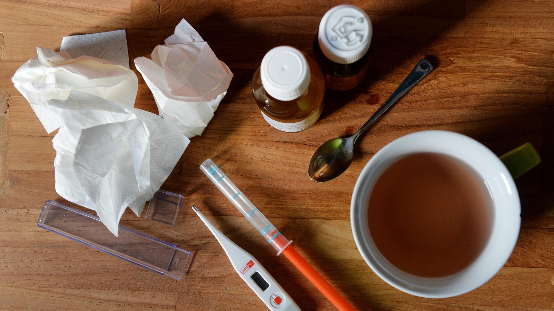 Auf einem Tisch liegen Medikamente, Taschentücher und ein Fieberthermometer