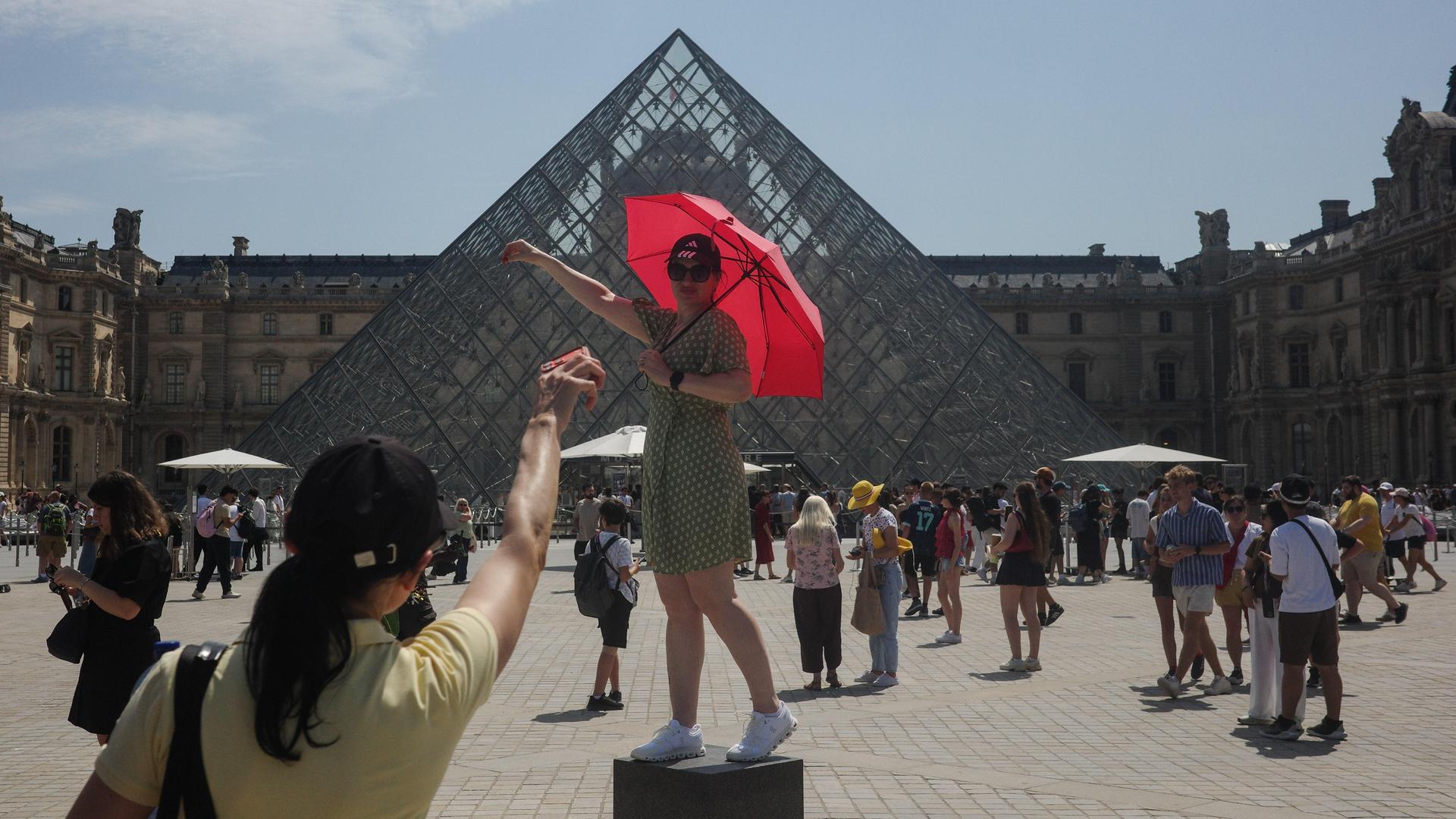 Touristen posieren vor der gläsernen Pyramide des Louvre mit einem Regenschirm als Sonnenschutz Touristen posieren vor der gläsernen Pyramide des Louvre mit einem Regenschirm als Sonnenschutz