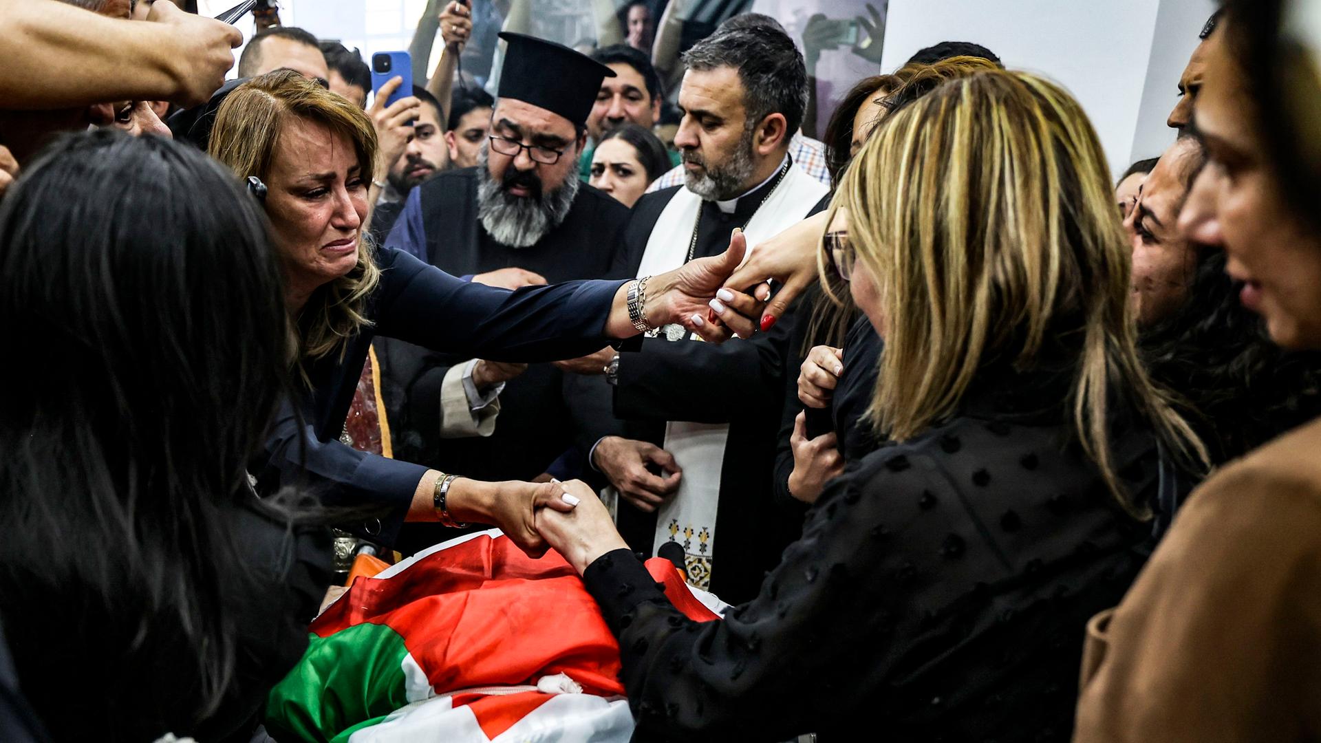 Palästinensische Autonomiegebiete, Ramallah: Eine Frau weint und reicht zwei anderen Frauen die Hände als der mit einer Flagge bedeckte Körper der getöteten Al-Dschasira-Journalistin Schirin Abu Akle in das Büro von Al-Dschasira gebracht wird.
