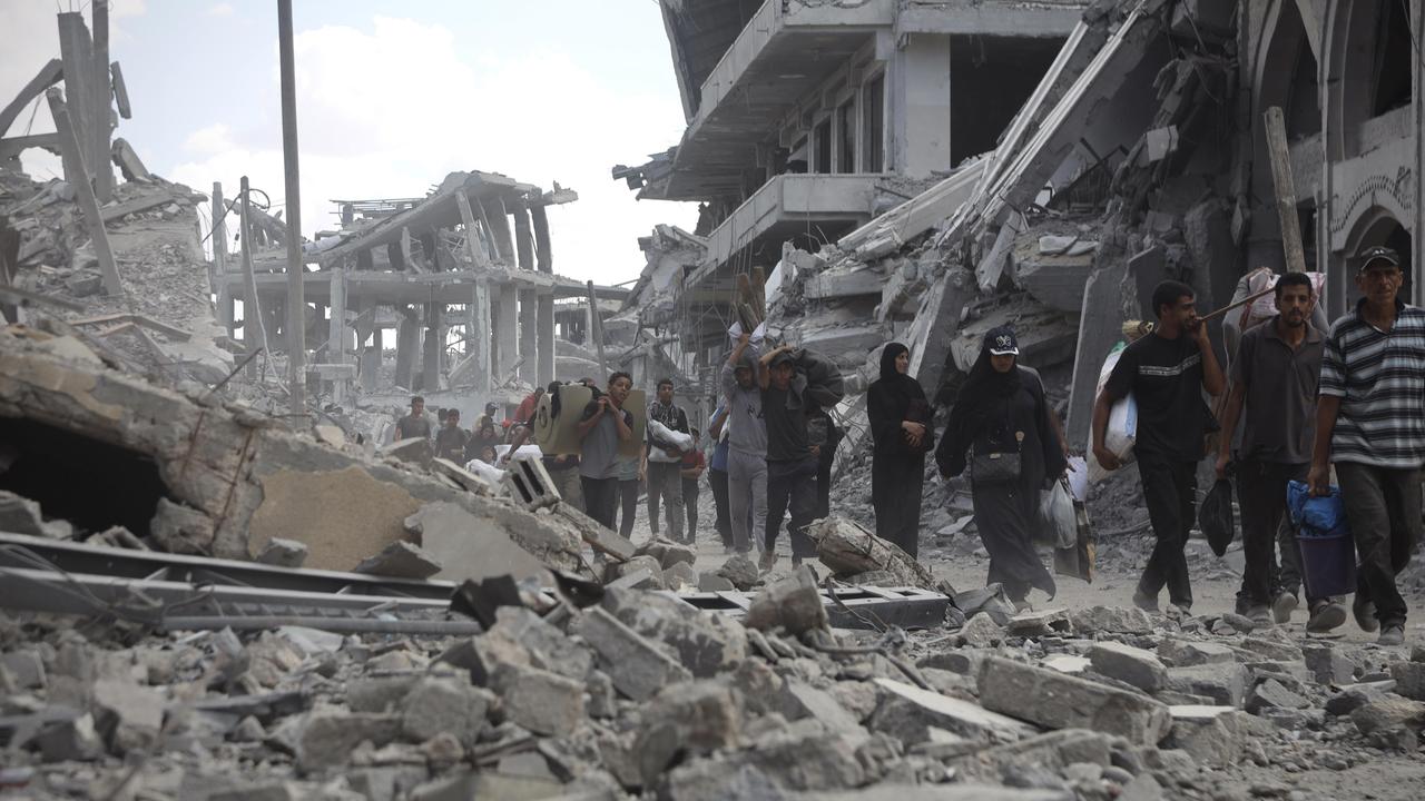 Mehrere Menschen laufen durch eine Straße voller Schutt und eingestürzter Gebäude. Im Hintergrund sind schwer beschädigte Betonbauten zu sehen. 