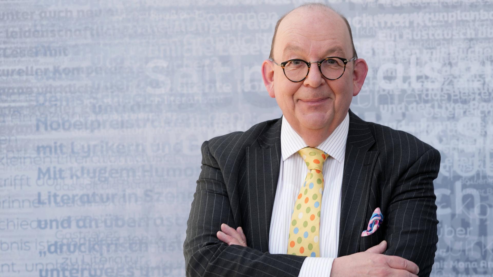 Denis Schek im Sakko mit bunter Krawatte und Einstecktuch auf einer Bühne der Leipziger Buchmesse Denis Schek im Sakko mit bunter Krawatte und Einstecktuch auf einer Bühne der Leipziger Buchmesse