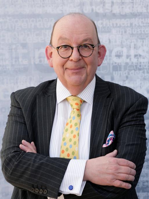 Denis Schek im Sakko mit bunter Krawatte und Einstecktuch auf einer Bühne der Leipziger Buchmesse