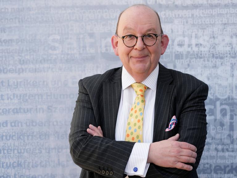 Denis Schek im Sakko mit bunter Krawatte und Einstecktuch auf einer Bühne der Leipziger Buchmesse