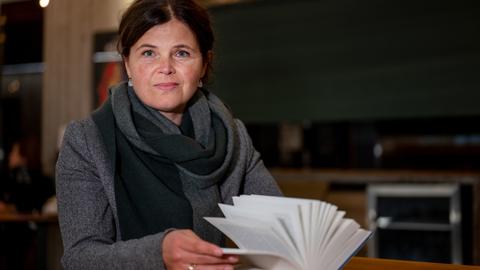 Die Schriftstellerin Julia Franck sitzt an einem Tisch vor einem geöffneten Buch. Sie blickt in die Kamera.