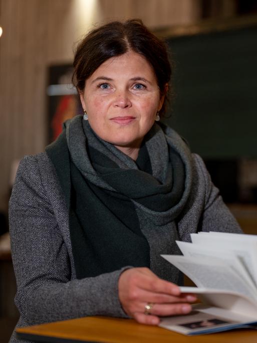 Die Schriftstellerin Julia Franck sitzt an einem Tisch vor einem geöffneten Buch. Sie blickt in die Kamera.