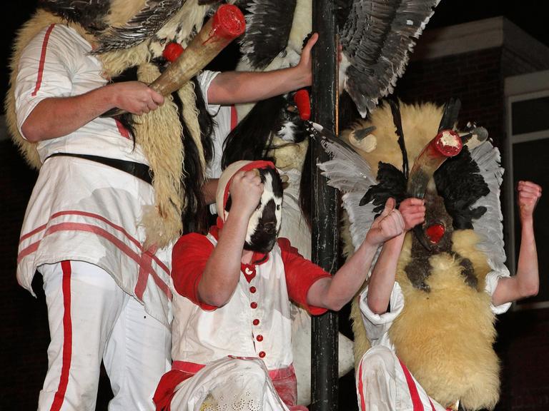 Mit Masken verkleidete Männer des Vereins "Borkumer Jungens" auf einer Litfaßsäule, sie schwenken Kuhhörner und tragen Felle und rot-weisse Kleidung.