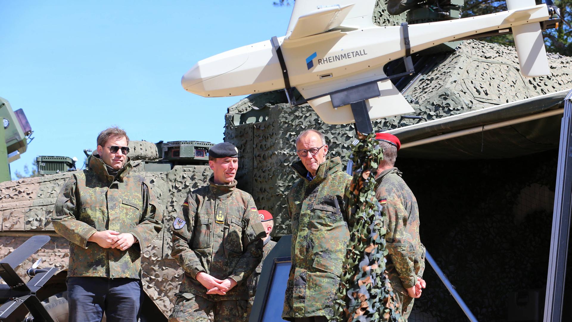 Bundeskanzler Merz und Vizekanzler Klingbeil werden vom Inspekteur des Heeres, Generalleutnant Christian Freudin über verschiedene Drohnen informiert. Links eine KI-gesteuerte XH-2-Drohne der Firma Helsing, rechts eine Drohne Raider FV-014 von Rheinmetall