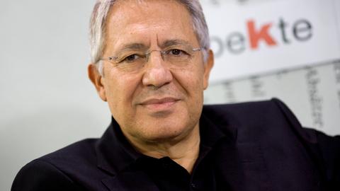 Ein Mann mit kurzem grauen Haar und randloser Brille lächelt verhalten in die Kamera. Er trägt ein schwarzes Hemd.