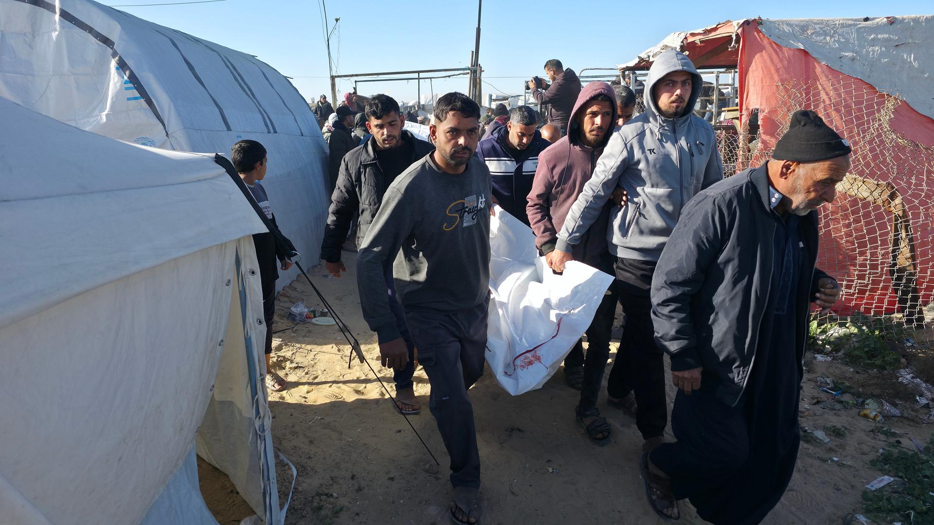 Männer tragen einen Leichensack durch die Zeltreihen in Chan Junis