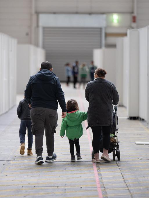 Eine Flüchtlingsfamilie geht durch eine zu einer Massenunterkunft umfunktionierten Messehalle in Frankfurt. In der Halle sind seit einigen Wochen mehrere hundert Migranten und Asylsuchende aus unterschiedlichen Herkunftsländern untergebracht.