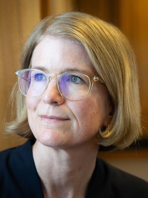 Porträt von Susanne Schwarzbach, aufgenommen im Funkhaus am Hans-Rosenthal-Platz. Sie trägt eine Brille mit hellem Rahmen, ein dunkles Oberteil und schaut leicht lächelnd zur Seite.