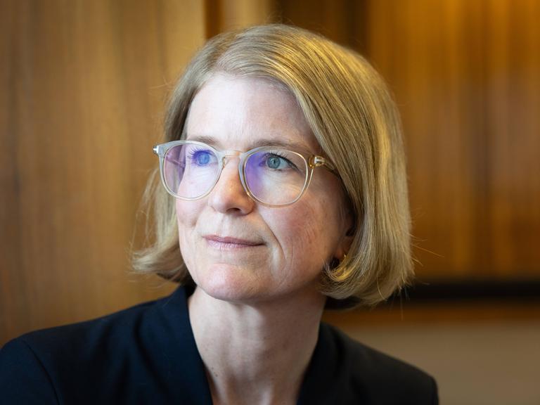 Porträt von Susanne Schwarzbach, aufgenommen im Funkhaus am Hans-Rosenthal-Platz. Sie trägt eine Brille mit hellem Rahmen, ein dunkles Oberteil und schaut leicht lächelnd zur Seite. Porträt von Susanne Schwarzbach, aufgenommen im Funkhaus am Hans-Rosenthal-Platz. Sie trägt eine Brille mit hellem Rahmen, ein dunkles Oberteil und schaut leicht lächelnd zur Seite.