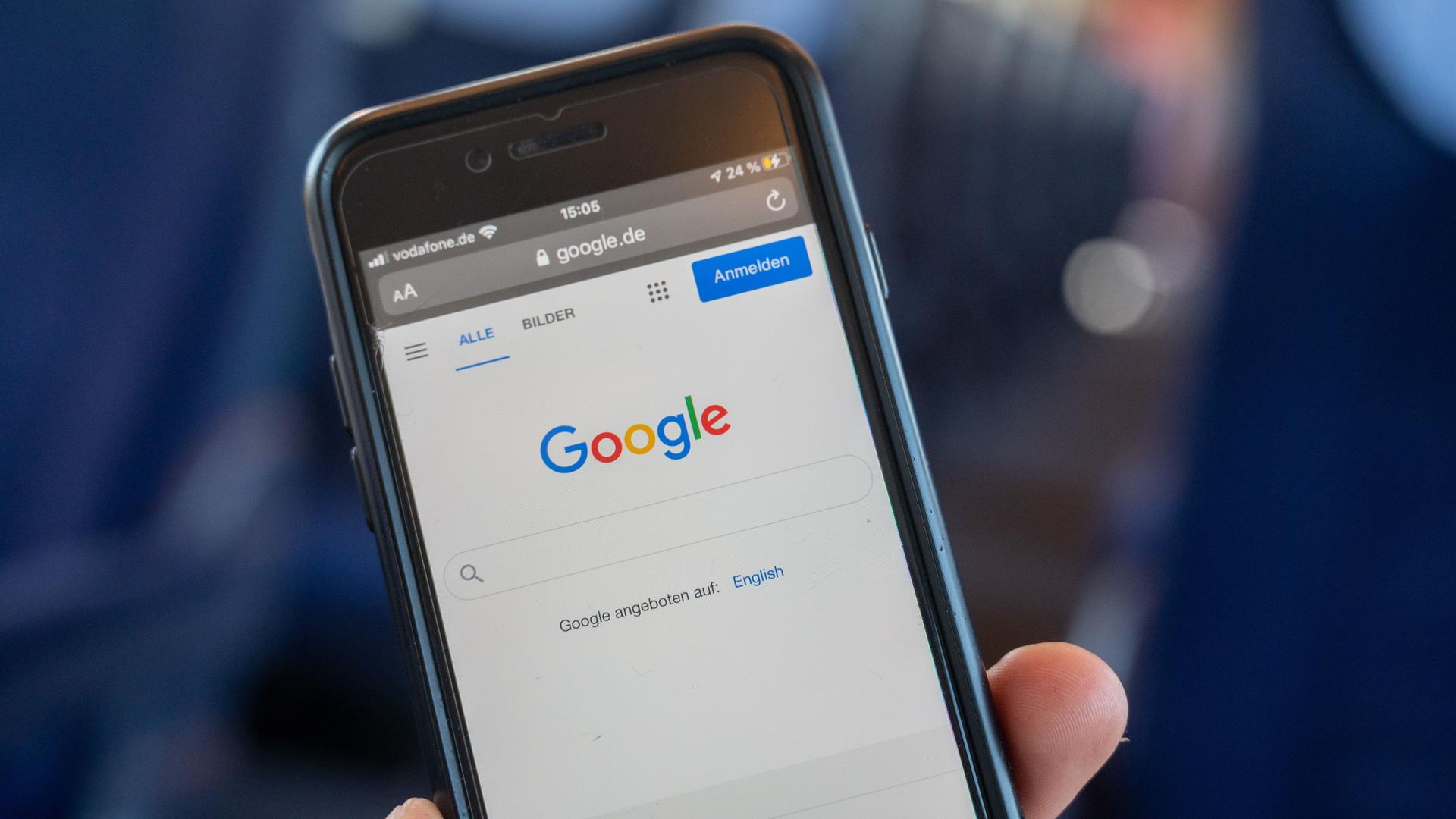 Ein Mann hält ein Handy in der Hand, auf dem die Google-Suche zu sehen ist. 