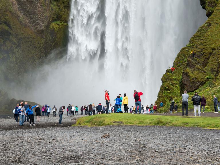 Touristengruppen stehen vor einem riesigen Wasserfall.